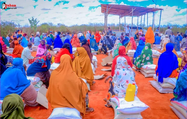 Families seated with sacks of food staples at a HARO distribution under an open sky