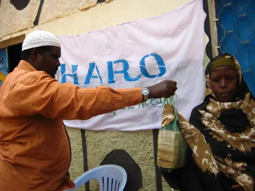 A HARO worker hands cash relief to an elderly woman under a HARO 'Empowering the Needy' banner in Buuhoodle, 2011