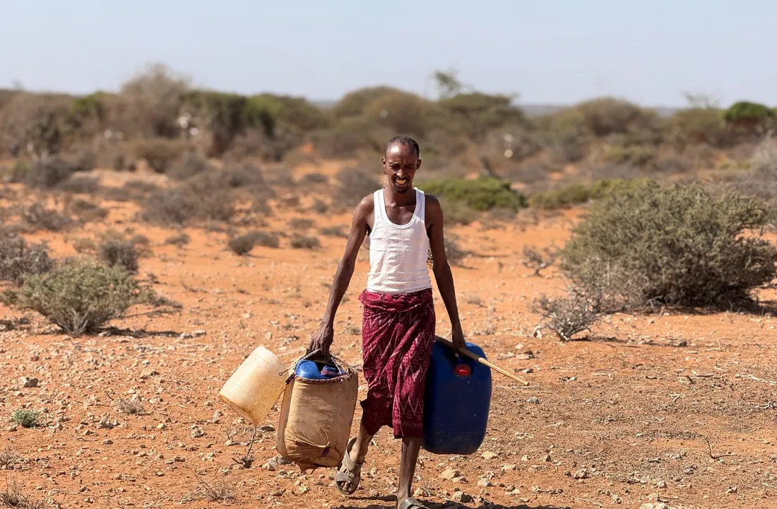 A man carries water containers home across dry scrubland in Somalia
