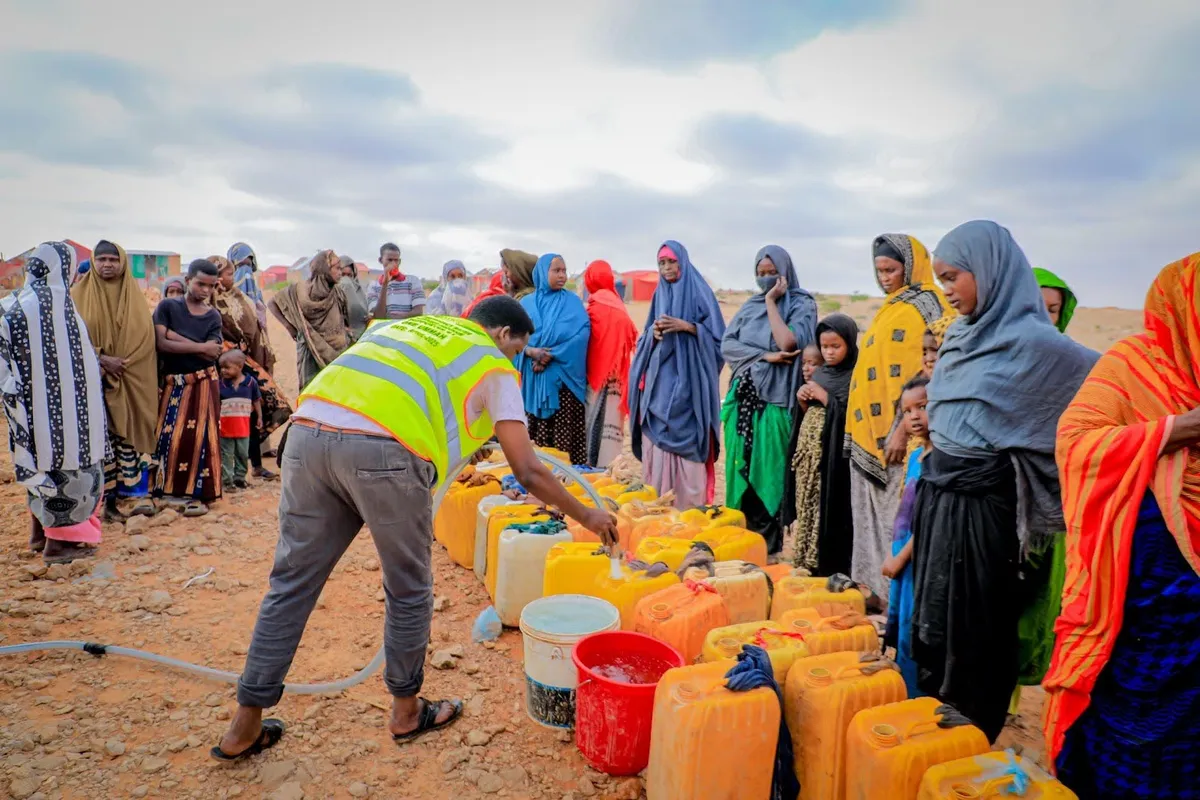 A HARO worker in a high-visibility vest fills families' jerry cans at a water distribution